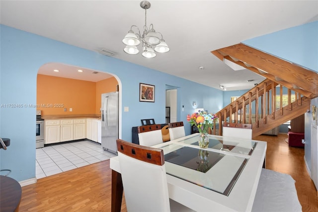 dining area with arched walkways, a notable chandelier, light wood finished floors, visible vents, and stairs