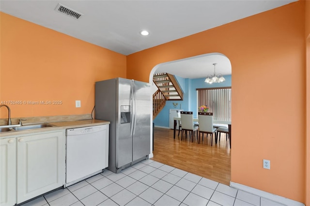 kitchen featuring light tile patterned floors, white dishwasher, a sink, visible vents, and stainless steel fridge