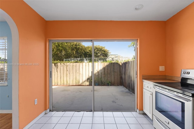 kitchen with stainless steel electric range oven, light tile patterned floors, arched walkways, and baseboards