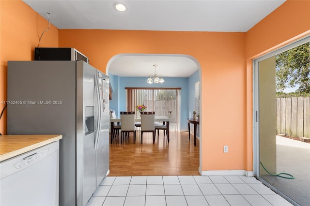 kitchen with a notable chandelier, light tile patterned floors, light countertops, stainless steel fridge, and dishwasher