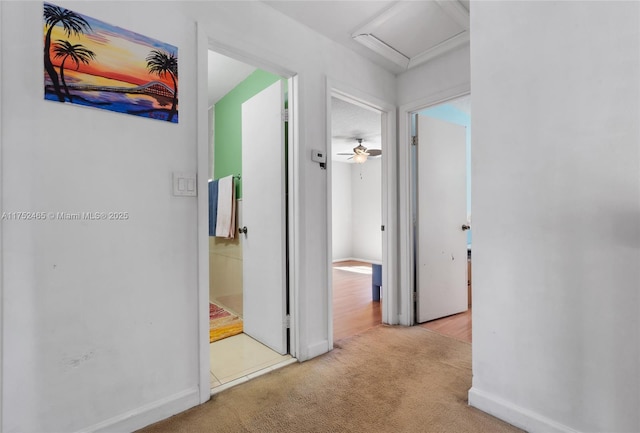 hall featuring attic access, carpet flooring, and baseboards