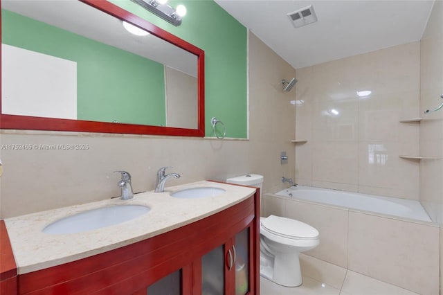 bathroom with toilet, tiled shower / bath, visible vents, and a sink