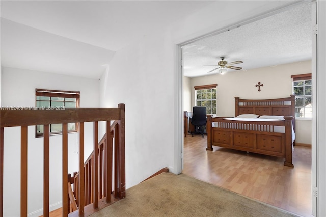 bedroom featuring a ceiling fan, multiple windows, a textured ceiling, and wood finished floors