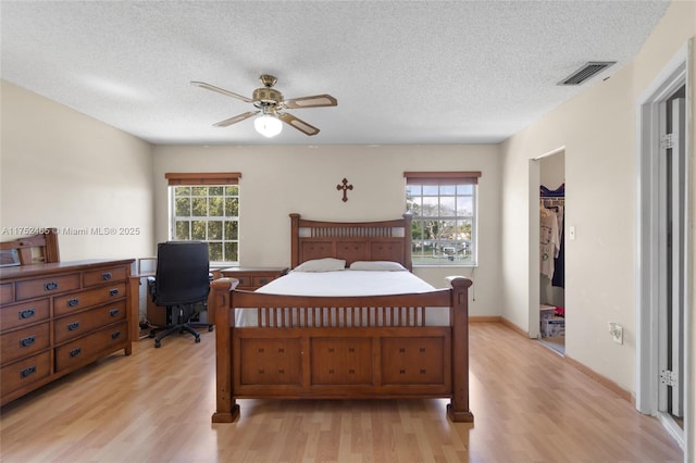 bedroom with light wood-type flooring, ceiling fan, a textured ceiling, and a spacious closet