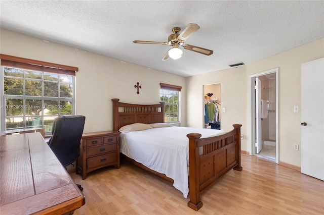 bedroom with visible vents, a spacious closet, light wood-style floors, a textured ceiling, and ensuite bath