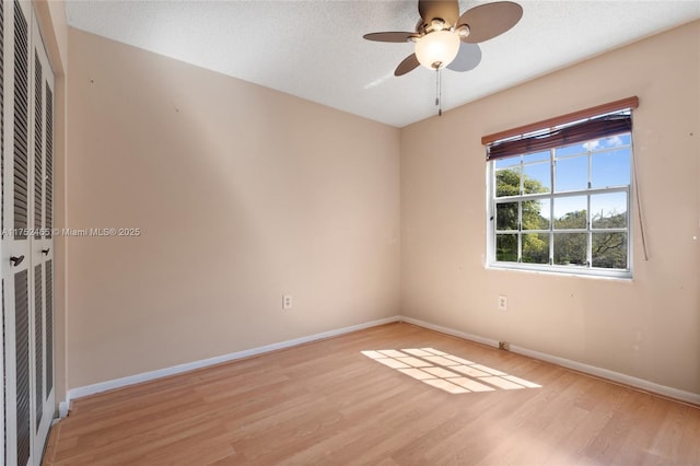 spare room with a textured ceiling, ceiling fan, light wood-style flooring, and baseboards