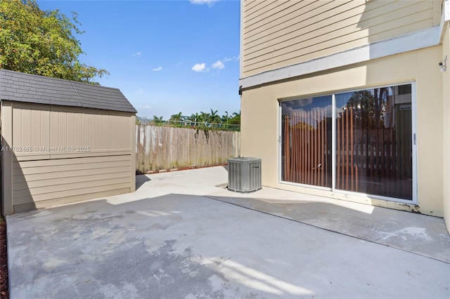 view of patio featuring central AC unit, a storage unit, fence, and an outbuilding