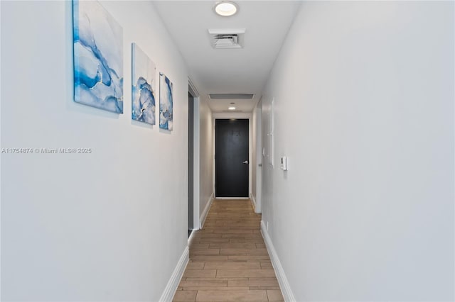 hallway with wood tiled floor, visible vents, and baseboards