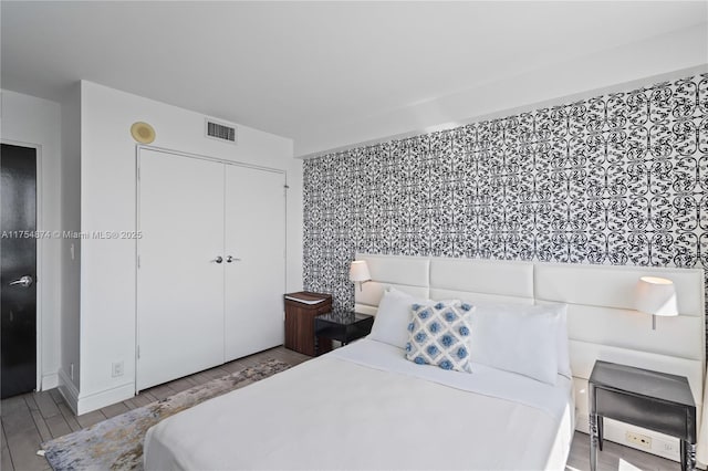 bedroom with wood tiled floor, a closet, and visible vents