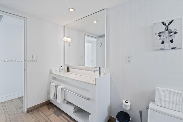 bathroom featuring toilet, recessed lighting, baseboards, and vanity