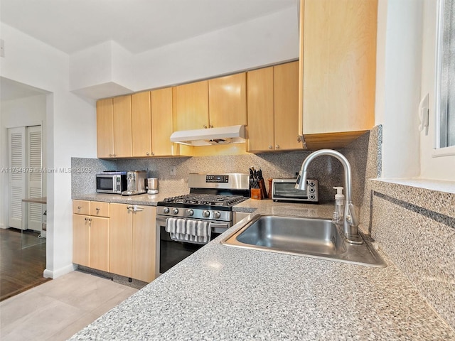 kitchen featuring stainless steel range with gas cooktop, backsplash, light brown cabinets, a sink, and under cabinet range hood