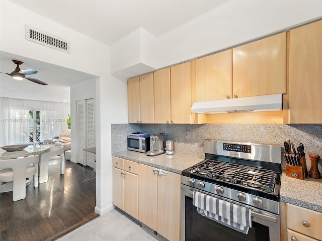 kitchen featuring under cabinet range hood, stainless steel appliances, visible vents, backsplash, and light brown cabinetry