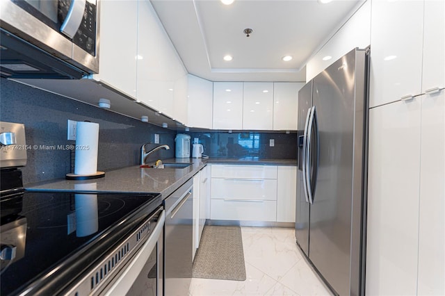 kitchen with a tray ceiling, marble finish floor, stainless steel appliances, white cabinetry, and modern cabinets