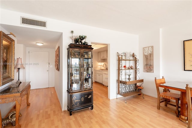 corridor featuring baseboards, a sink, visible vents, and light wood-style floors