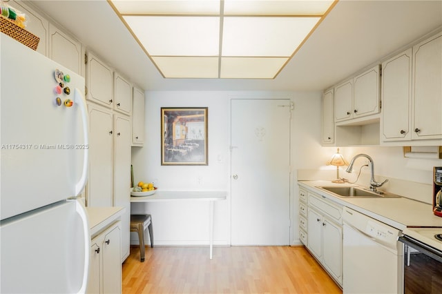 kitchen featuring light wood finished floors, light countertops, white appliances, and a sink
