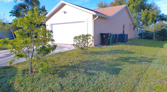 view of side of home with a yard, stucco siding, concrete driveway, central AC, and a garage