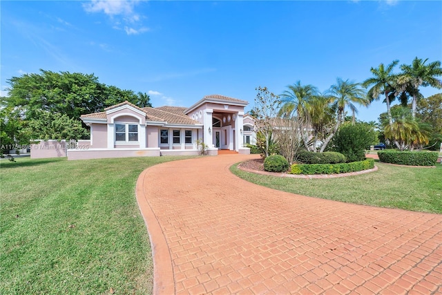 mediterranean / spanish-style home featuring a tiled roof, decorative driveway, a front yard, and stucco siding