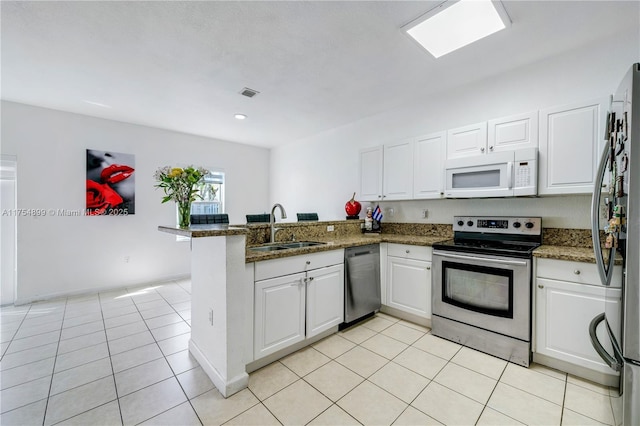 kitchen with light tile patterned floors, white cabinets, appliances with stainless steel finishes, a peninsula, and a sink