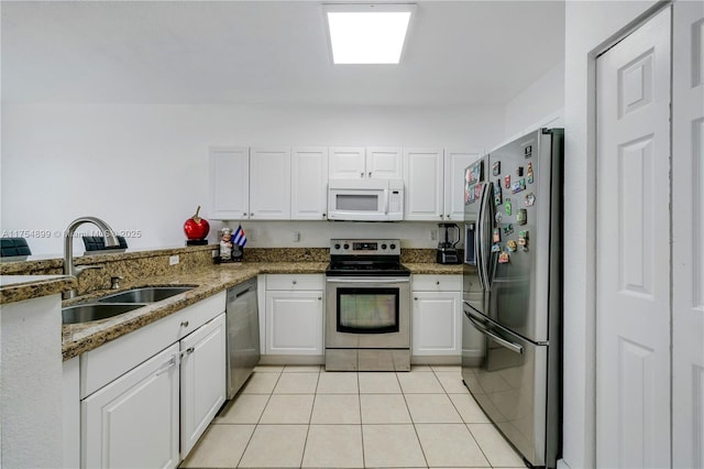 kitchen featuring light tile patterned floors, stainless steel appliances, stone counters, white cabinetry, and a sink