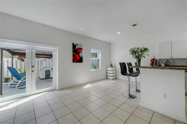 interior space featuring light tile patterned floors, visible vents, white cabinets, french doors, and a kitchen bar