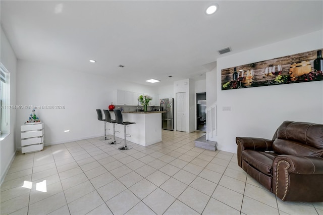 kitchen with a breakfast bar, stainless steel refrigerator with ice dispenser, visible vents, open floor plan, and a peninsula