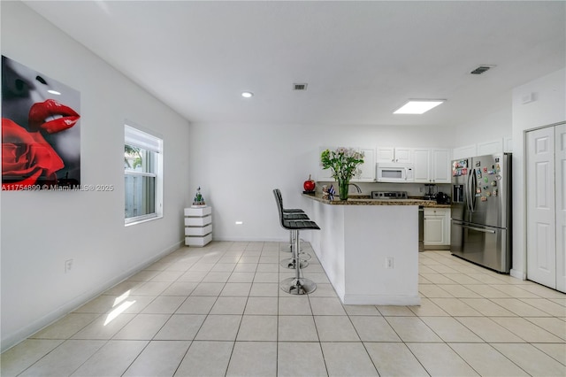 kitchen featuring light tile patterned floors, white microwave, a peninsula, white cabinets, and stainless steel fridge with ice dispenser