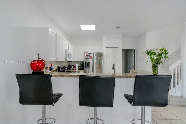 kitchen with visible vents, appliances with stainless steel finishes, a peninsula, a kitchen bar, and white cabinetry