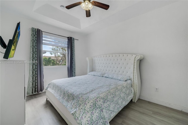 bedroom featuring a raised ceiling, ceiling fan, baseboards, and wood finished floors