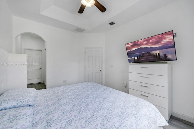 bedroom with arched walkways, a tray ceiling, wood finished floors, and visible vents