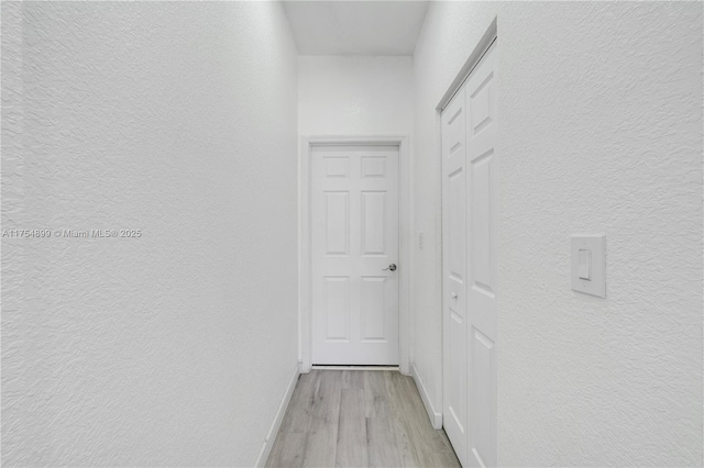 corridor featuring a textured wall, light wood-type flooring, and baseboards