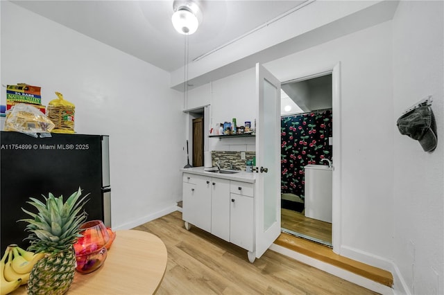 interior space with baseboards, backsplash, freestanding refrigerator, light wood-type flooring, and a sink