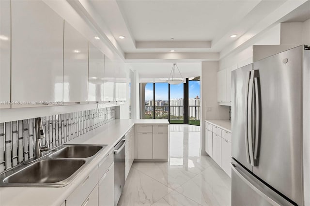 kitchen with a sink, white cabinets, appliances with stainless steel finishes, decorative backsplash, and a tray ceiling