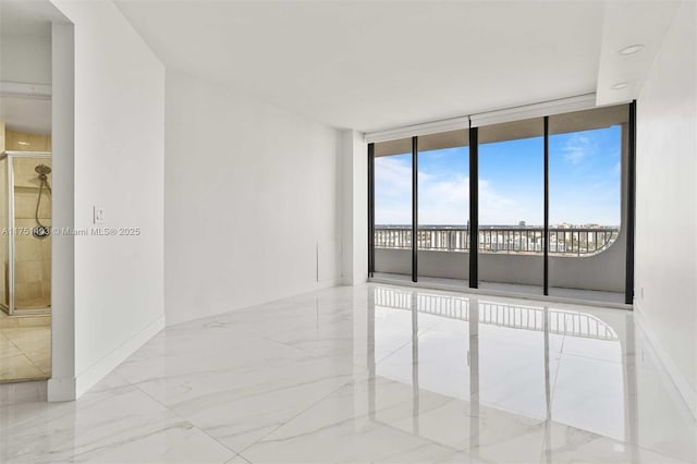 spare room featuring marble finish floor, a wall of windows, and baseboards