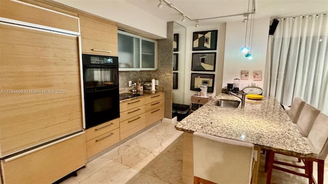 kitchen featuring light brown cabinetry, a peninsula, a sink, and black appliances