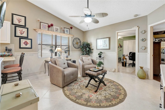 living area featuring light tile patterned floors, wainscoting, lofted ceiling, ceiling fan, and a textured ceiling