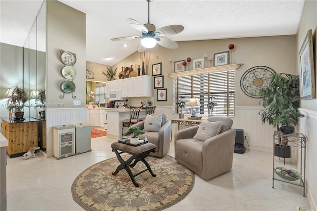 living area with light tile patterned floors, lofted ceiling, wainscoting, ceiling fan, and a textured ceiling