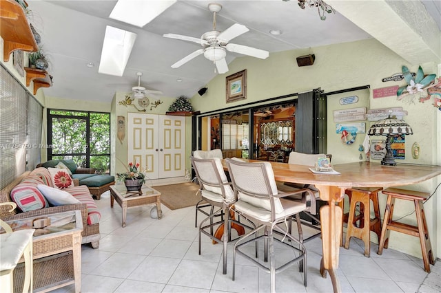 dining room with light tile patterned floors, vaulted ceiling with skylight, and ceiling fan