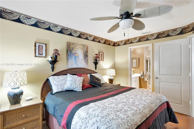bedroom with a textured ceiling, ensuite bath, wood finished floors, and visible vents