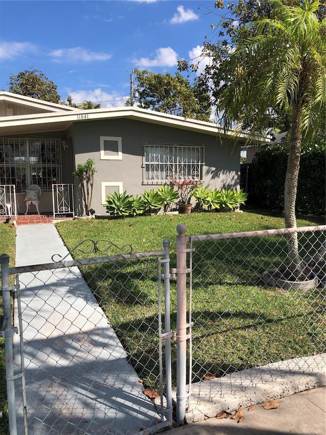 view of front of property with a gate, fence, a front lawn, and stucco siding