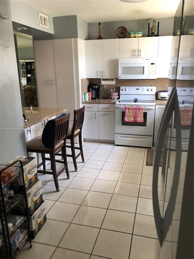 kitchen with light tile patterned floors, white appliances, visible vents, white cabinets, and tasteful backsplash