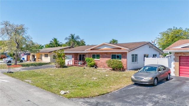 ranch-style house with driveway, brick siding, a front yard, and fence