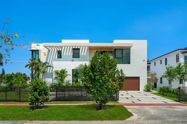 contemporary home featuring decorative driveway, fence, an attached garage, and stucco siding