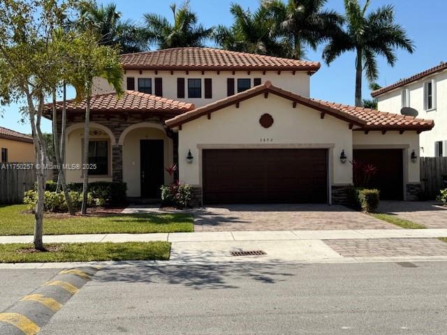 mediterranean / spanish house featuring stucco siding, decorative driveway, stone siding, fence, and a garage