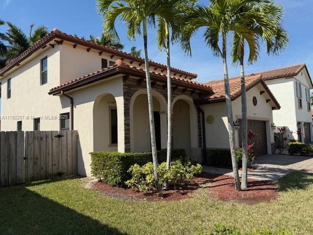 mediterranean / spanish-style home with a front lawn, fence, stucco siding, a garage, and driveway