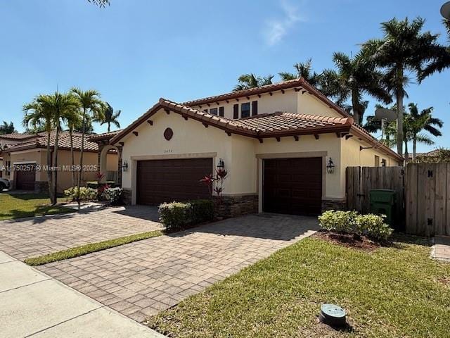 mediterranean / spanish-style home featuring fence, stucco siding, a garage, stone siding, and decorative driveway