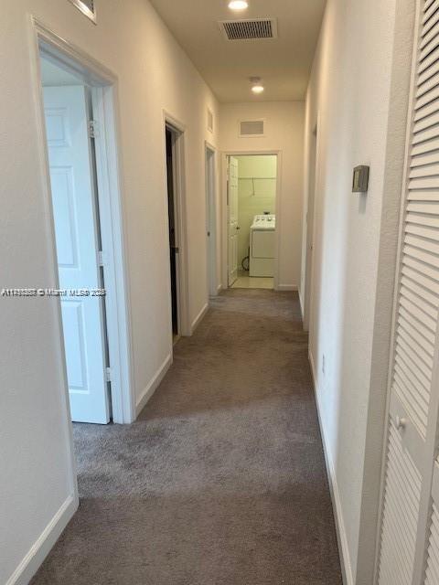 corridor featuring washer / dryer, baseboards, visible vents, and carpet floors