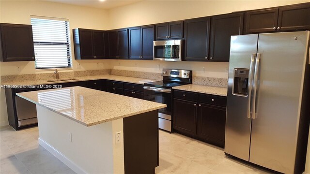 kitchen with light tile patterned floors, light stone countertops, a sink, appliances with stainless steel finishes, and a center island