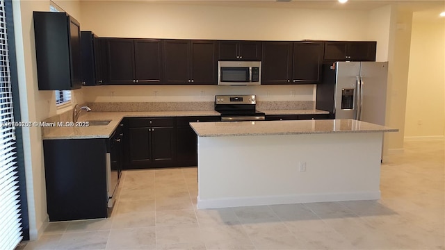 kitchen featuring a sink, light stone countertops, appliances with stainless steel finishes, and a center island