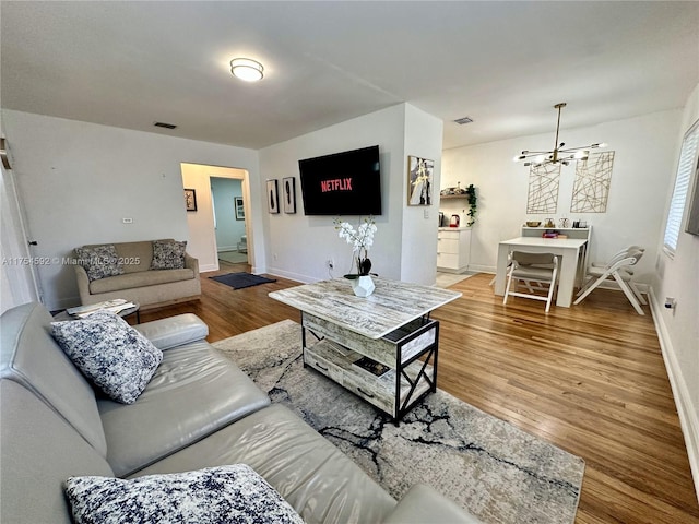 living room featuring baseboards, visible vents, a chandelier, and wood finished floors