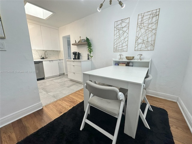 dining area with a skylight, baseboards, and light wood finished floors